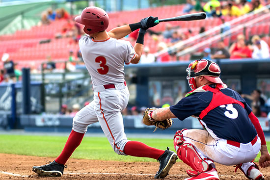 Baseball batter swinging during game with catcher behind home plate in stadium.