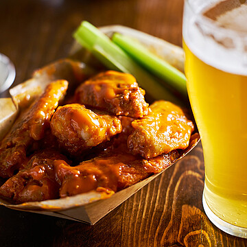 Spicy chicken wings with celery sticks and beer on a rustic wooden table.