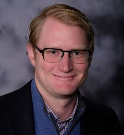 Smiling young professional in glasses and blazer, radiating warmth and confidence.