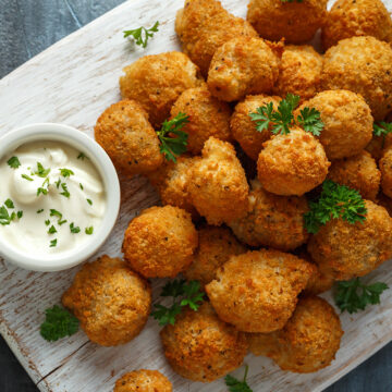 Crispy golden bites with creamy herb dip, garnished with parsley on a rustic board.