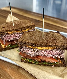 Hearty rye sandwich with savory meat, melted cheese, and fresh tomato slices.
