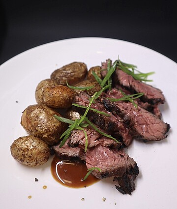 Savory medium-rare beef slices with golden roasted baby potatoes and vibrant sauce garnish.