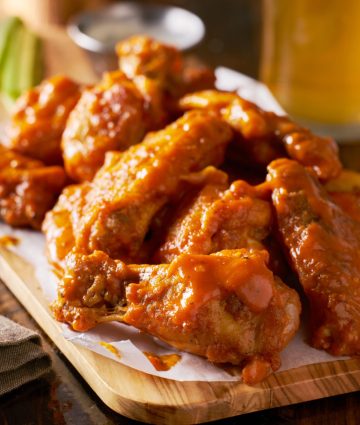 Spicy buffalo chicken wings served with celery and beer on a rustic wooden board.