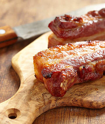 Delicious caramelized pork belly served on a rustic wooden board, ready to indulge.