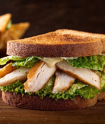 Savory chicken Caesar sandwich on toasted rye bread, topped with fresh romaine and creamy dressing.