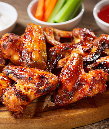 Succulent grilled chicken wings on a rustic wooden board with assorted dipping sauces.