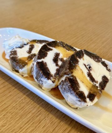 Decadent chocolate cream roll cake slices drizzled with caramel and served with whipped cream.