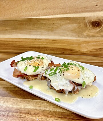 Crispy bacon topped with poached eggs and creamy sauce, garnished with green onions.