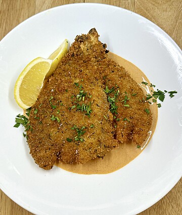 Crispy breaded fish topped with creamy sauce and a refreshing lemon wedge.