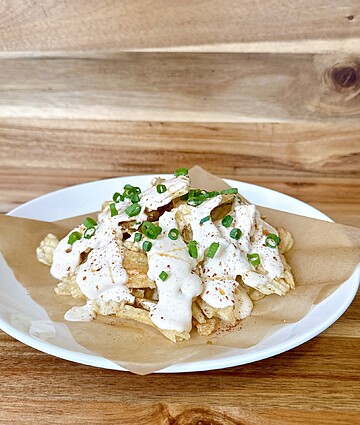 Delicious crispy fries topped with creamy sauce and fresh scallions, served on a rustic plate.