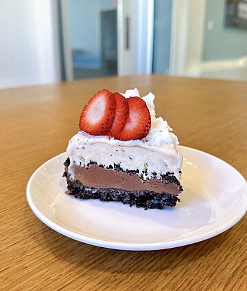 Luxurious layered chocolate cake topped with whipped cream and fresh strawberries on a wooden table.