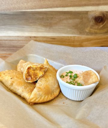 Savory golden empanadas with a creamy dipping sauce on rustic wooden background.