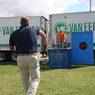 Man throwing ball at dunk tank during Van Eerden food distributor promotional event, showcasing B2B foodservice company engagement.