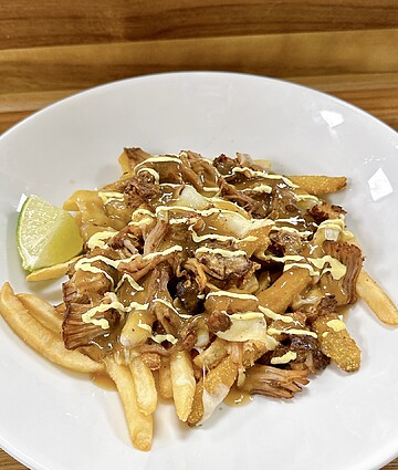 Delicious loaded fries topped with pulled meat, tangy sauce, and fresh lime wedge.