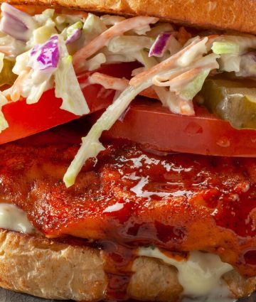 Savory fried chicken sandwich with spicy sauce, coleslaw, and fresh toppings on a toasted bun.
