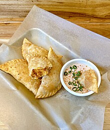 Golden fried empanadas with creamy spicy dipping sauce on parchment-lined tray.
