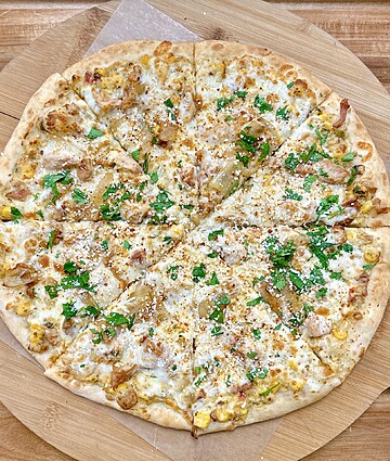 Gourmet chicken and corn pizza, perfectly baked, on a rustic wooden board.