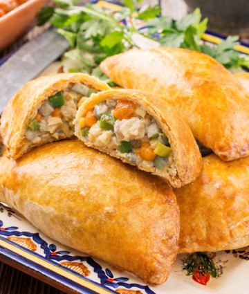 Golden vegetable empanadas on rustic plate with flaky crust and savory filling.