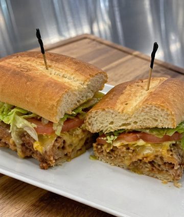 Two premium beef burgers with melted cheese, fresh lettuce, tomato, and caramelized onions on artisan rolls, plated for commercial foodservice.