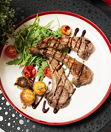 Grilled lamb chops with roasted potatoes, salad, and balsamic glaze for fine dining elegance.