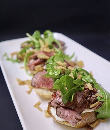 Delicious gourmet beef sliders topped with crispy onions and fresh greens on a stylish platter.