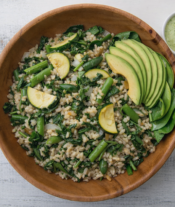 Healthy grain bowl with avocado, spinach, zucchini, and green vegetables on wooden background.