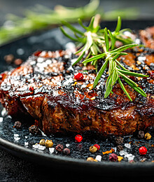 Juicy grilled steak topped with rosemary and colorful peppercorns on a sleek black plate.