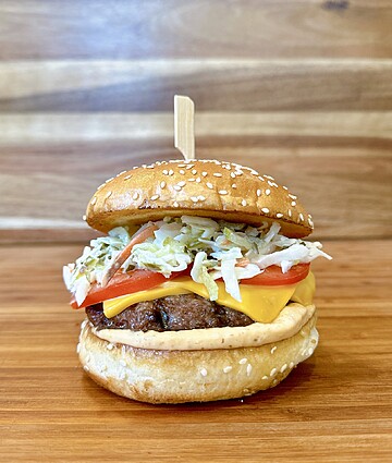 Delicious hamburger with fresh ingredients and melted cheddar on a rustic wooden backdrop.