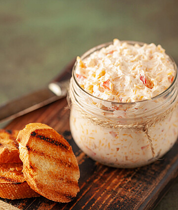 Savory pimento cheese bruschetta served with toasted baguette slices on a rustic wooden board.