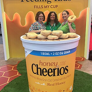 Large promotional Honey Cheerios bulk cereal container at foodservice trade show, demonstrating portion control and grain serving sizes for institutional food distribution.