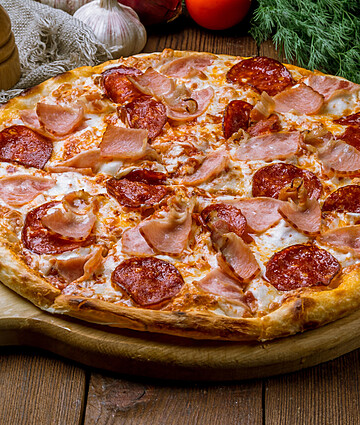 Gourmet Italian meat pizza with pepperoni, ham, and mozzarella on a rustic wooden board.