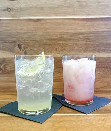 Refreshing lemon and strawberry iced drinks on wooden table with ice and citrus garnish.