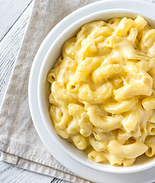 Decadent gourmet macaroni and cheese served in a white bowl on a rustic wooden surface.