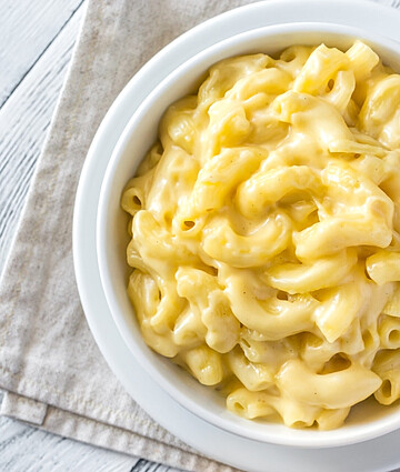 Decadent gourmet macaroni and cheese served in a white bowl on a rustic wooden surface.