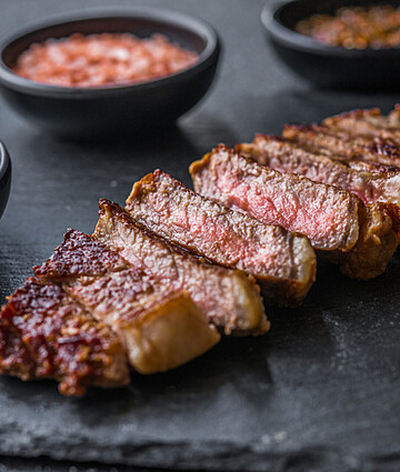 Sliced medium-rare beef steak with herb crust and gourmet spice rubs, perfect for fine dining and wholesale food service distribution.