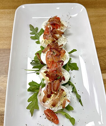 Mozzarella, cherry tomatoes, and bacon salad with arugula and black pepper garnish.