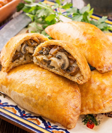 Golden mushroom and onion hand pies on colorful ceramic platter with rustic wooden background.