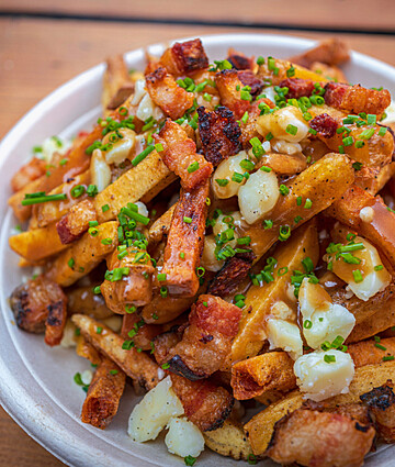 Decadent poutine topped with crispy pork belly and cheese curds on golden fries.