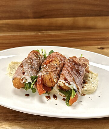 Delicious prosciutto-wrapped rolls filled with arugula and roasted peppers, drizzled with balsamic reduction.