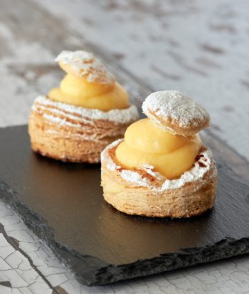 Delicious puff pastry cakes with creamy filling, elegantly presented on a black plate.