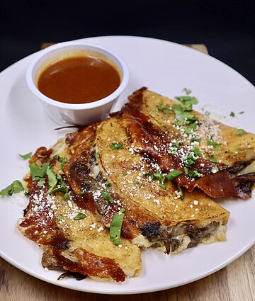 Golden quesadillas with fresh cilantro and salsa, served on a rustic wooden surface.