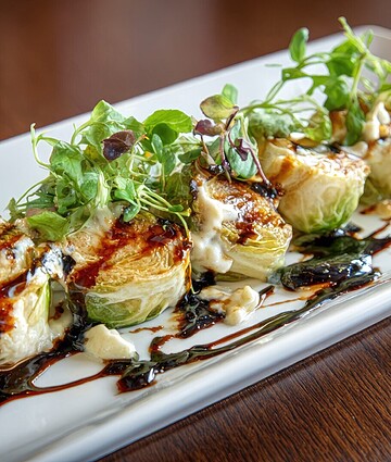 Gourmet roasted Brussels sprouts skewers with balsamic glaze and fresh herbs on a white plate.