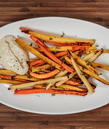 Vibrant roasted root vegetables served with a creamy dip on a rustic wooden background.