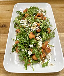 Colorful arugula salad with roasted vegetables and creamy cheese on a rustic wooden table.