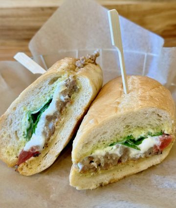 Delicious sandwich with fresh vegetables, savory meat, and creamy spread on rustic parchment.
