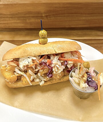 Colorful hoagie sandwich with fried seafood and creamy coleslaw on a white plate.