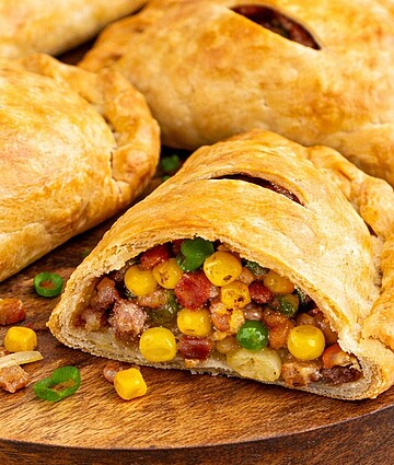 Golden baked hand pies filled with seasoned meat, corn, peas, and potatoes on wooden board—perfect for wholesale food distribution and commercial foodservice.