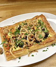 Delicious vegetable pastry topped with crispy onions and a creamy sauce, elegantly presented.
