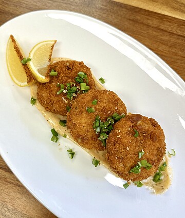 Crispy seafood fritters served with lemon wedges and creamy sauce on a rustic plate.
