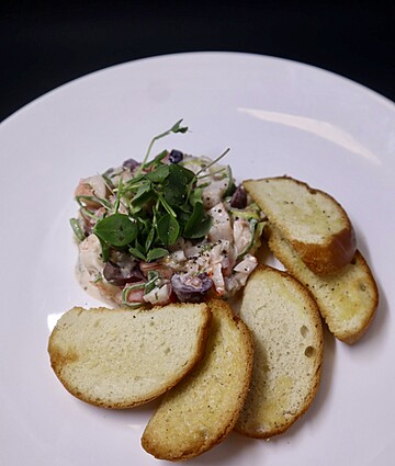 Colorful seafood salad with shrimp, fresh herbs, and crispy toasted bread on a white plate.